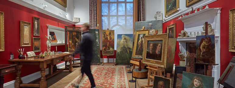 A red room with many paintings on wooden easels, a visitor walks past