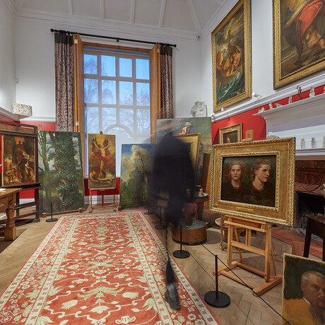 A blurred visitor in the gallery, there are white and red walls and paintings on easels