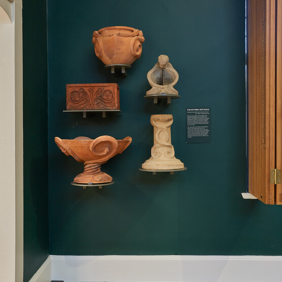 A green wall with five terracotta pottery pieces mounted