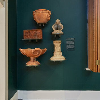 A green wall with five terracotta pottery pieces mounted