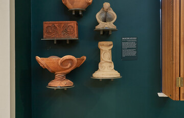 A green wall with five terracotta pottery pieces mounted