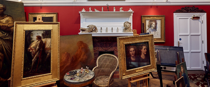 A white and red walled studio space with paintings on the wall and on easels