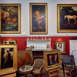 A white and red walled studio space with paintings on the wall and on easels