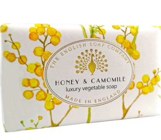 A bar of honey and camomile soap in it's packaging featuring yellow camomile illustrations