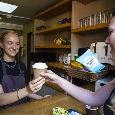 A staff member in the Watts Tea Shop hands a hot drink to a customer whilst smiling