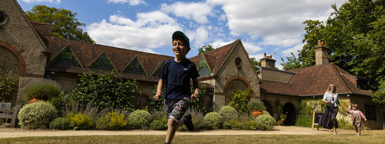 Family running in front of Watts Gallery building on the lawn