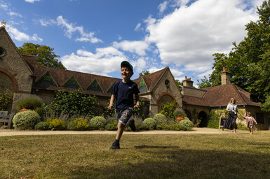 Family running in front of Watts Gallery building on the lawn