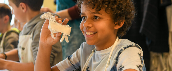 A young boy holds up a horse he's made out of tin foil and smiles