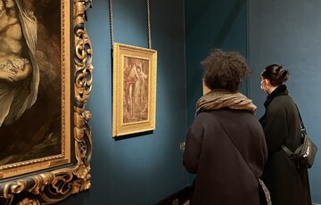 Two visitors with their backs to camera view a gold-framed painting in the blue-walled Historic Gallery