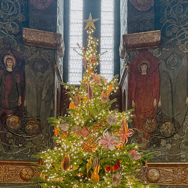 A decorated Christmas tree stands in a decorative Arts and Crafts chapel
