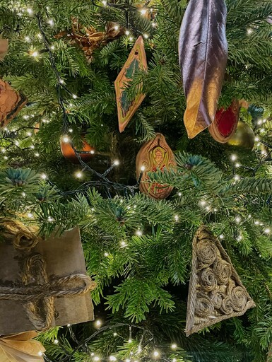 Close-up photograph of a Christmas tree. Decorating the tree are fairy lights, hand painted terracotta decorations and other decorations made out of paper and card.