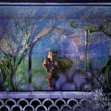 Photo of Clytie bust sculpture at Watts Gallery lit up with purple light in the evening